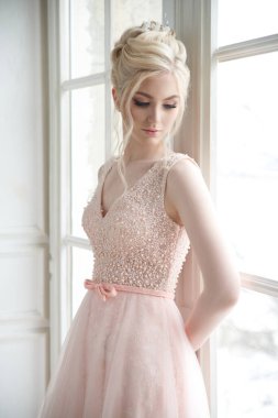 Pencerenin yanında zarif saçlı, pembe elbiseli güzel bir kız gelin..