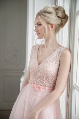 Pencerenin yanında zarif saçlı, pembe elbiseli güzel bir kız gelin..