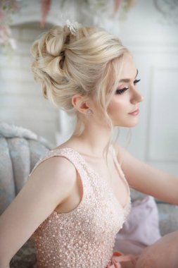 Güzel kız zarif bir saç elbisesi ve zarif pembe bir elbisesi olan gelin şık bir iç mekanda oturuyor..