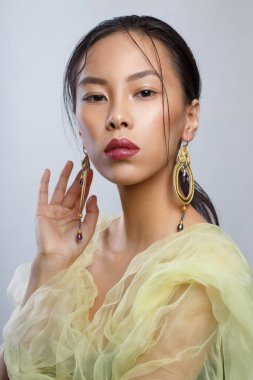 Güzel Asyalı bir kızın zarif portresi. Büyük zarif küpeleri ve sarı havadar kıyafetleri var..