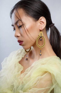 Güzel Asyalı bir kızın zarif portresi. Büyük zarif küpeleri ve sarı havadar kıyafetleri var..