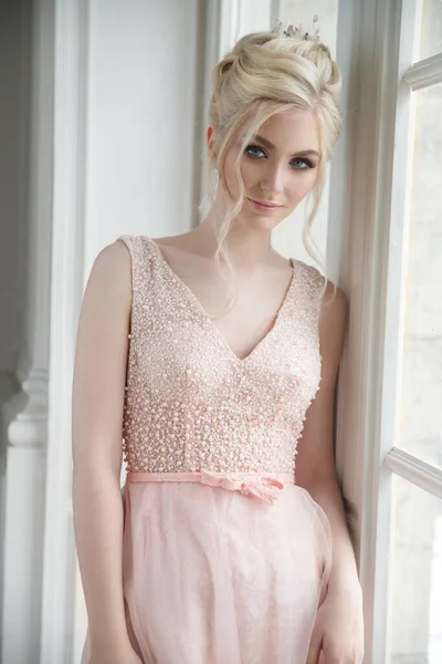 Beautiful girl bride with elegant hair in a gently pink dress near the window.