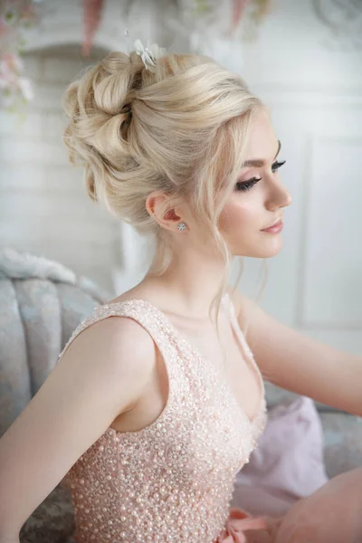 Güzel kız zarif bir saç elbisesi ve zarif pembe bir elbisesi olan gelin şık bir iç mekanda oturuyor..