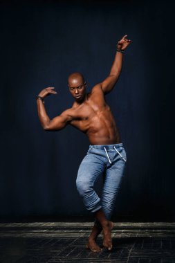 Kotlu, çıplak gövdeli siyah bir atletik arka planda dans ediyor..