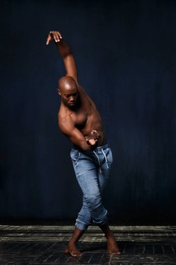 Kotlu, çıplak gövdeli siyah bir atletik arka planda dans ediyor..