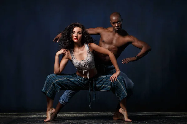 A slender white girl and an athletic black man in a graceful dance against a dark blue background.