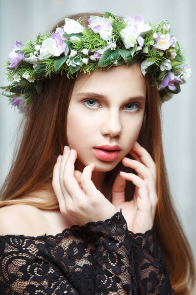 Portrait of a young beautiful girl with a delicate wreath on her head indoors.