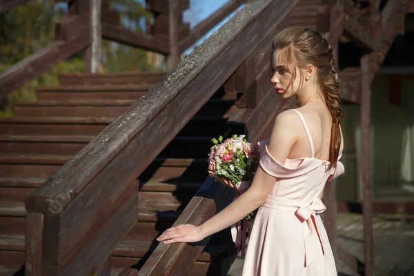 一位年轻的新娘 身穿精致的粉色连衣裙 手里拿着一束鲜花 站在乡村的阳台上 她的半身画像 — 图库照片