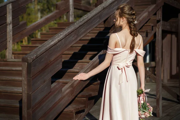 一个年轻的新娘穿着精致的粉红婚纱 手里拿着一束鲜花 站在乡村的阳台上 站在夏日的背面 她的画像 — 图库照片
