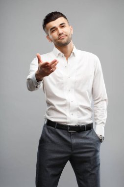 Yakışıklı sıradan bir adam, bir kolunu ileri uzatıyor. Gri bir arka planda tek başına..