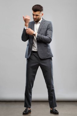 Zarif takım elbiseli genç şık bir adam kelepçelerini takıyor, tamamen büyümüş, gri bir arka planda soyutlanmış..