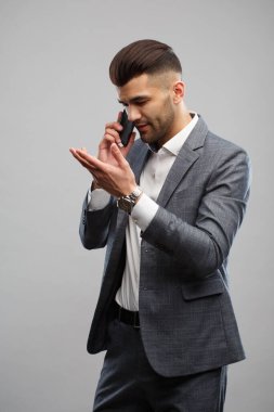 Zarif takım elbiseli şık bir genç telefonda konuşuyor. Gri bir arka planda elleri izole bir şekilde el kol hareketi yapıyor..