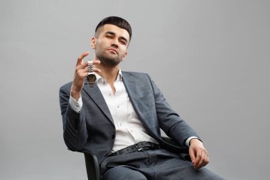 Takım elbiseli çekici bir Asyalı elinde tuttuğu bir kol saati gösteriyor. Gri bir arka planda izole edilmiş..