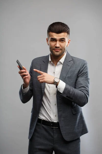 양복을 남자가 손에는 스마트폰을 손에는 그것을 가리키면서 배경에 고립되어 — 스톡 사진