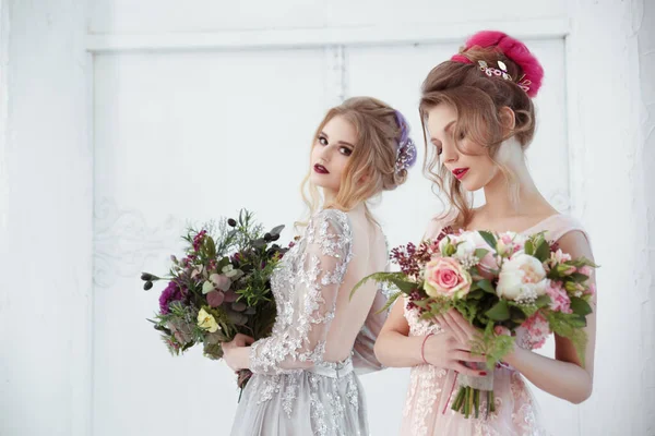 Two bride girls with hairdos with colored strands holding bouquets of flowers in their hands.