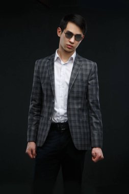 Siyah arka planda güneş gözlüklü, takım elbiseli genç Asyalı adam izole edilmiş..