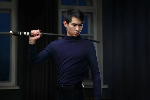 Young Asian man with a sword in his hands in a dark room.