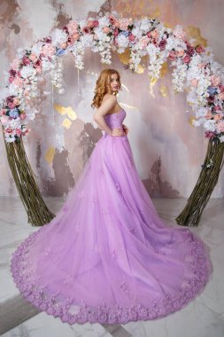 Çiçek kemerinin altında bir trenle uzun, gür leylak bir elbise içinde zarif bir gelin..