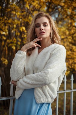 Parktaki altın sonbahar yeşilliklerinin arka planında rahat beyaz kürklü tatlı sarışın bir kızın portresi..