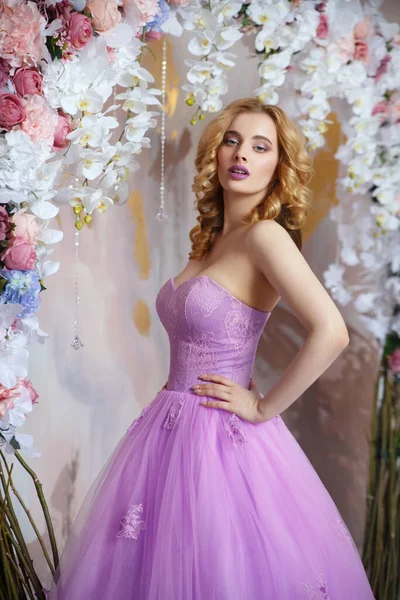 美しいです女の子ブロンドでスマートなライラックドレスと化粧花から装飾的なアーチの近くの色のコスト — ストック写真