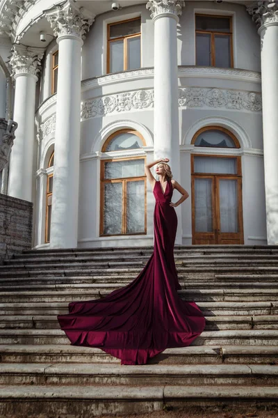美丽纤细的姑娘 身穿深红色的丝质连衣裙 在皇宫的台阶上坐着一列长列火车 — 图库照片