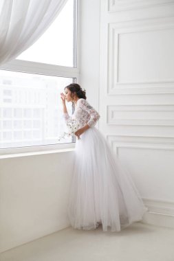 Güzel, zarif bir gelinin portresi. Parlak bir iç mekanda, pencerenin yanında bekliyor..