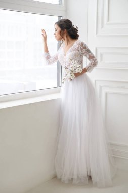 Güzel, zarif bir gelinin portresi. Parlak bir iç mekanda, pencerenin yanında bekliyor..