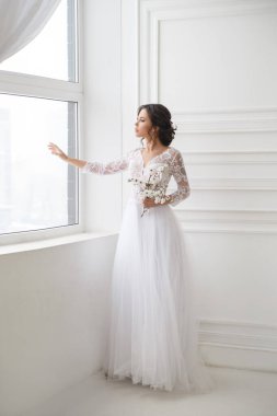 Güzel, zarif bir gelinin portresi. Parlak bir iç mekanda, pencerenin yanında bekliyor..