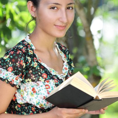 Asyalı görünümlü güzel bir kadın açık havada kitap okuyor.