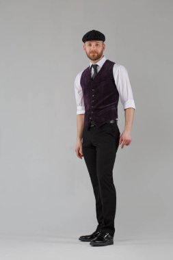 Gri arka planda izole edilmiş şık giyinmiş, uzun boylu, sakallı bir adam..