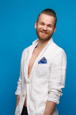 Mavi arka planda beyaz keten ceketli, sakallı, zarif, gülen adam..