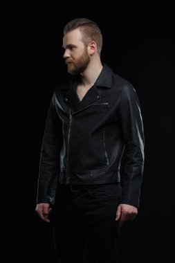 Siyah deri ceketli sevimli sakallı adam siyah arka planda izole edilmiş..