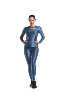 Mavi metalik spor giysili ince esmer kadın beyaz arka planda tamamen yalıtılmış bir şekilde duruyor..