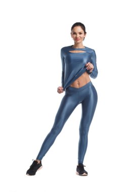 Mavi metalik spor giysili ince esmer kadın beyaz arka planda tamamen yalıtılmış bir şekilde duruyor..