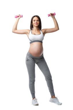 İnce atletik hamile kız, beyaz arka planda izole bir şekilde ayakta duran halterlerle spor yapıyor..
