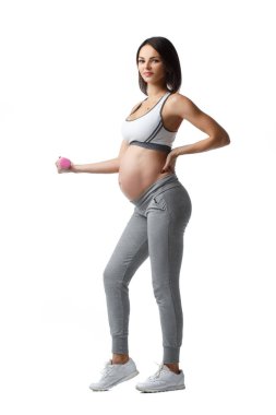 İnce atletik hamile kız, beyaz arka planda izole bir şekilde ayakta duran halterlerle spor yapıyor..