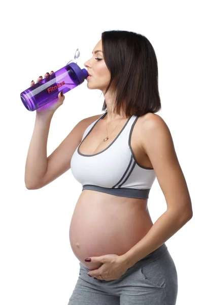 瘦小的运动孕妇穿着运动服喝水被白色背景隔离 — 图库照片