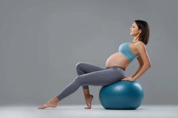 瘦小的运动怀孕女孩在一个灰色背景的球上健身 — 图库照片