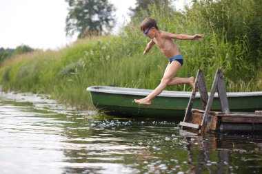 Kırsal bir arazinin arka planında uçan bir çocuk suya atlıyor..