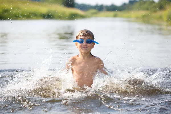 夏の日に水泳をしながら水の中でゴーグルの幸せな子供が飛び散ったり戯れたり — ストック写真