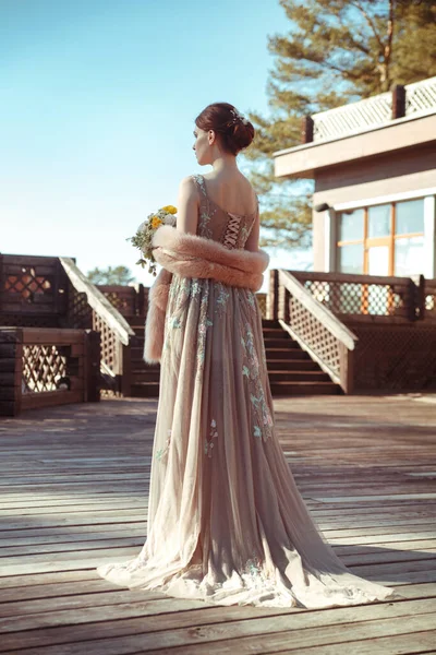 Portrait of an elegant bride in an unusual flowing dress view from the back on the hotel terrace.