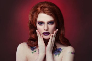 Kırmızı arka planda yaratıcı gece makyajıyla parlak kızıl saçlı bir kızın güzel portresi..