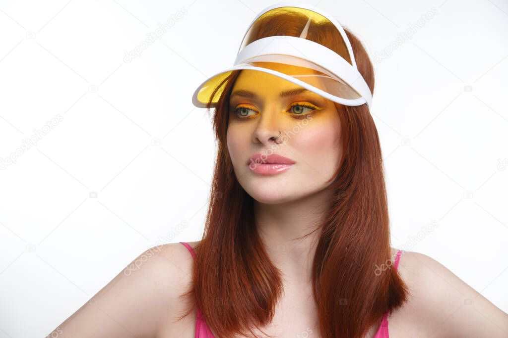 Portrait of a sexy red-haired girl in a transparent yellow sun visor isolated on a white background.