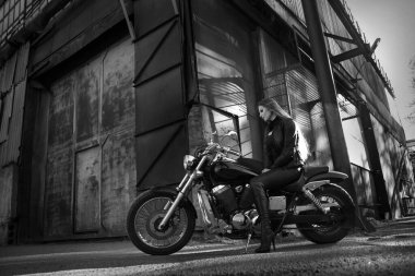 Endüstriyel bir caddede motosikletli güzel bir kızın siyah beyaz fotoğrafı..