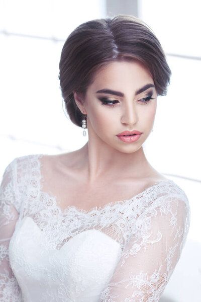 Portrait of a beautiful bright brunette bride with downcast eyes in lace dress