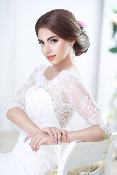 Portrait of a beautiful brunette bride flirty makeup and hairstyle in lace in the interior