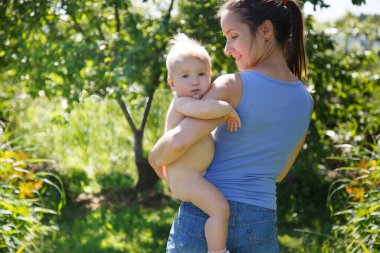 Anne, sıcak bir yaz gününde kucağında tombul bir bebek tutuyor..