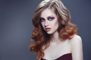 Gri bir arka planda, şık bukleli ve parlak makyajlı seksi bir kızın güzel portresi..