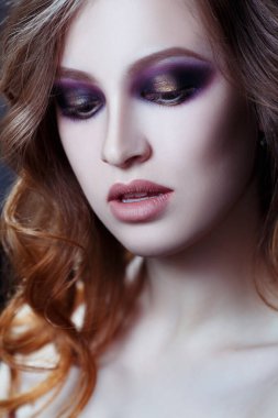 Gri bir arka planda, şık bukleli ve parlak makyajlı seksi bir kızın güzel portresi..