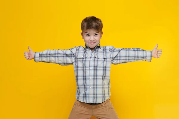 穿着格子呢衬衫的小男孩很可爱 他的两臂高高地伸出一个大拇指 伸出来的两边都是黄色的背景 — 图库照片